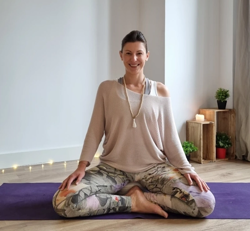 Claudia Schriever sitzt auf Yoga-Matte und Mediationskissen. Sie hat eine Mala-Kette umgehängt.