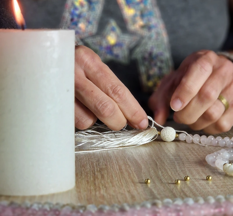 Eine Mala-Kette wird gebastelt, eine Kerze leuchtet im Vordergrund.